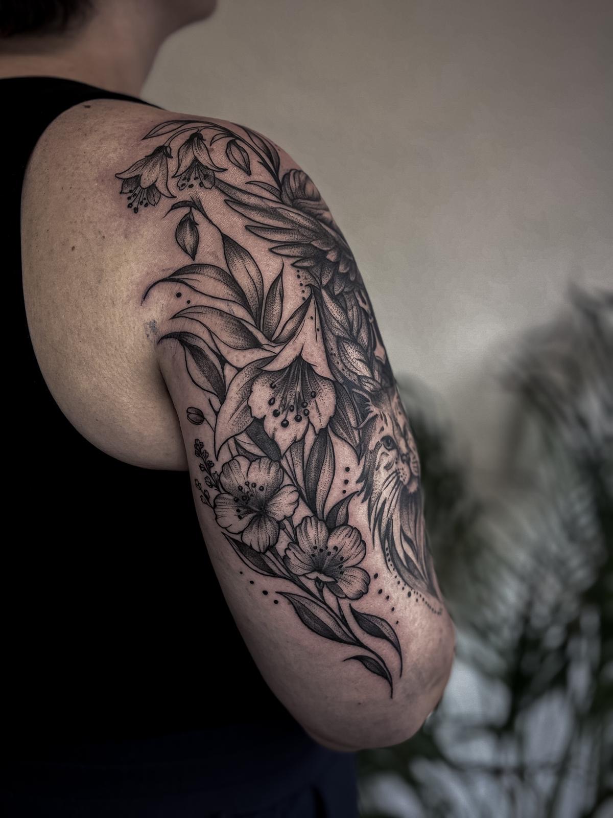 Florales Oberarm-Tattoo mit fein schattierten Blüten und Blättern